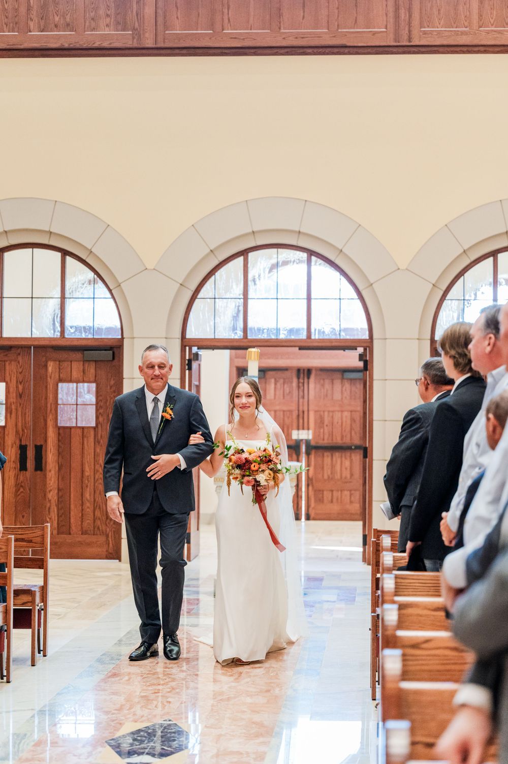 Bride walks down the aisle with her dad during her wedding at OSU's St. John Catholic Student Center in Stillwater, Oklahoma.