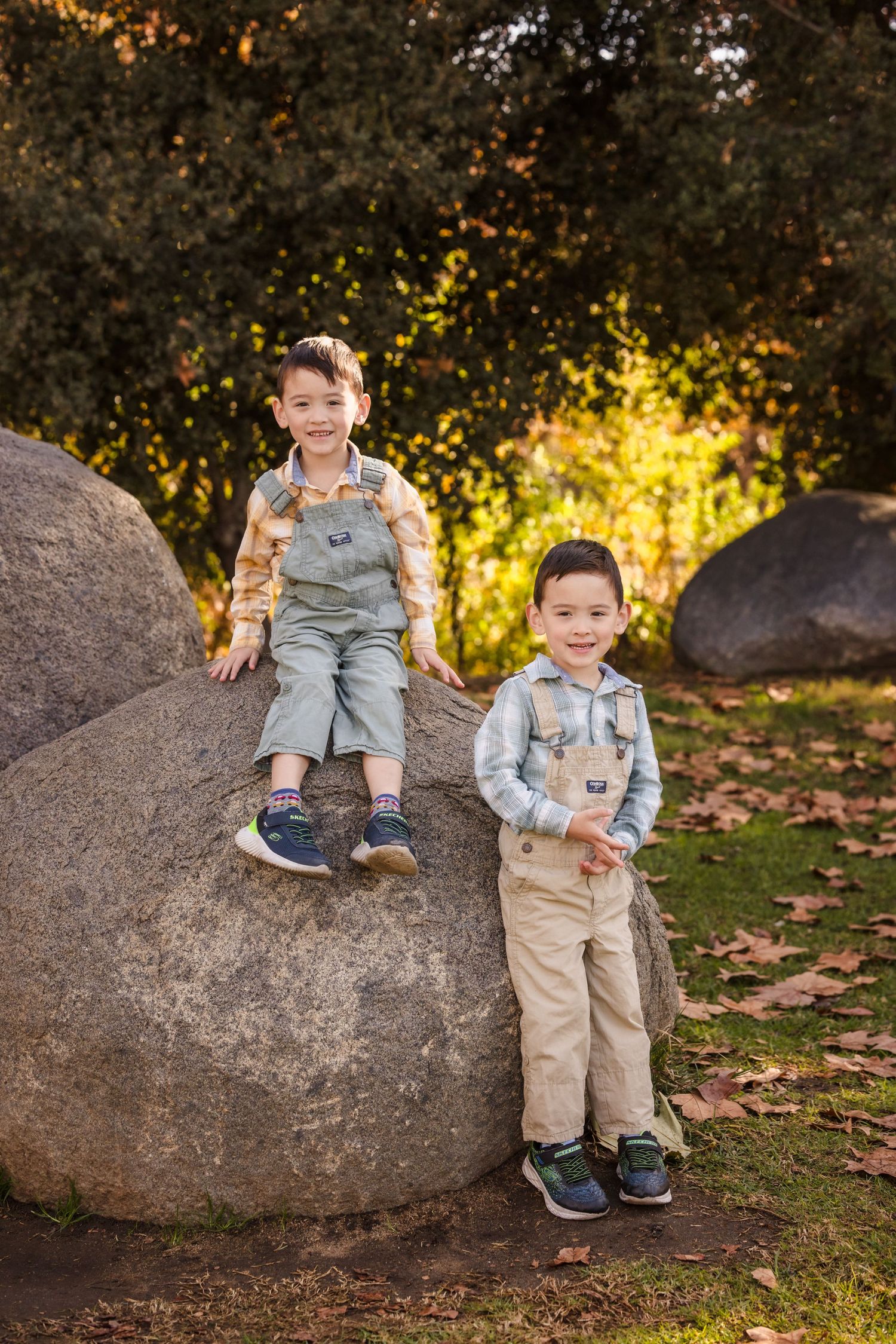 Two children pose on large rocks in an autumn garden setting with golden light.