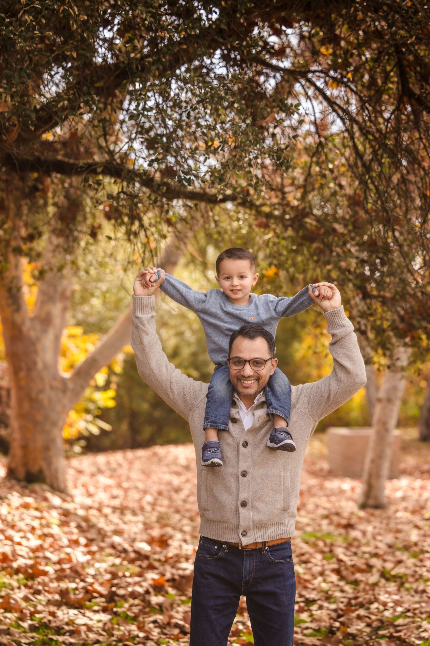 A joyful father lifts his child onto his shoulders amid autumn leaves.