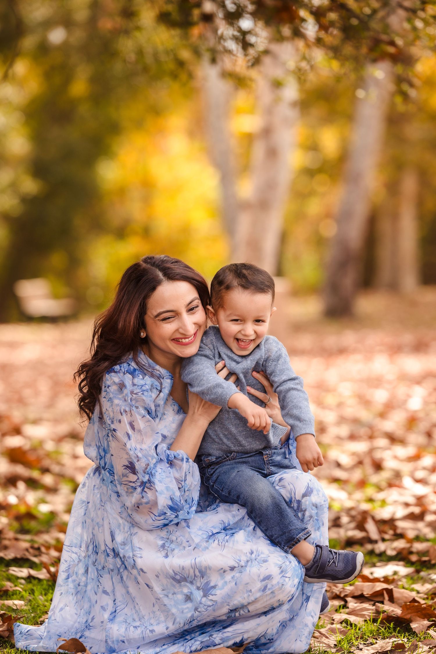 Mother and child share joyful moment together while sitting on autumn leaves in a park setting.