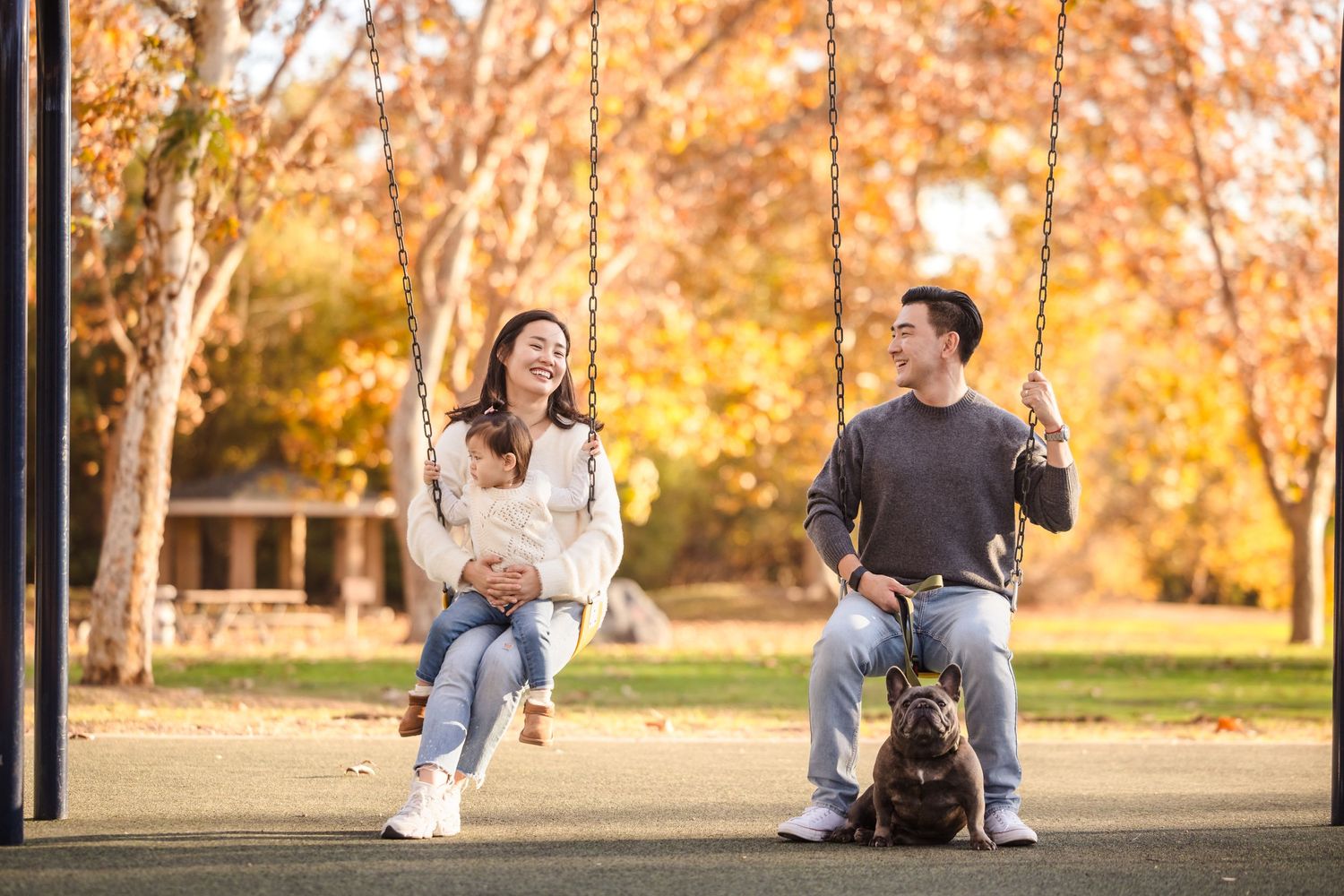A couple and their dog spend time together on swings at a playground during golden hour.