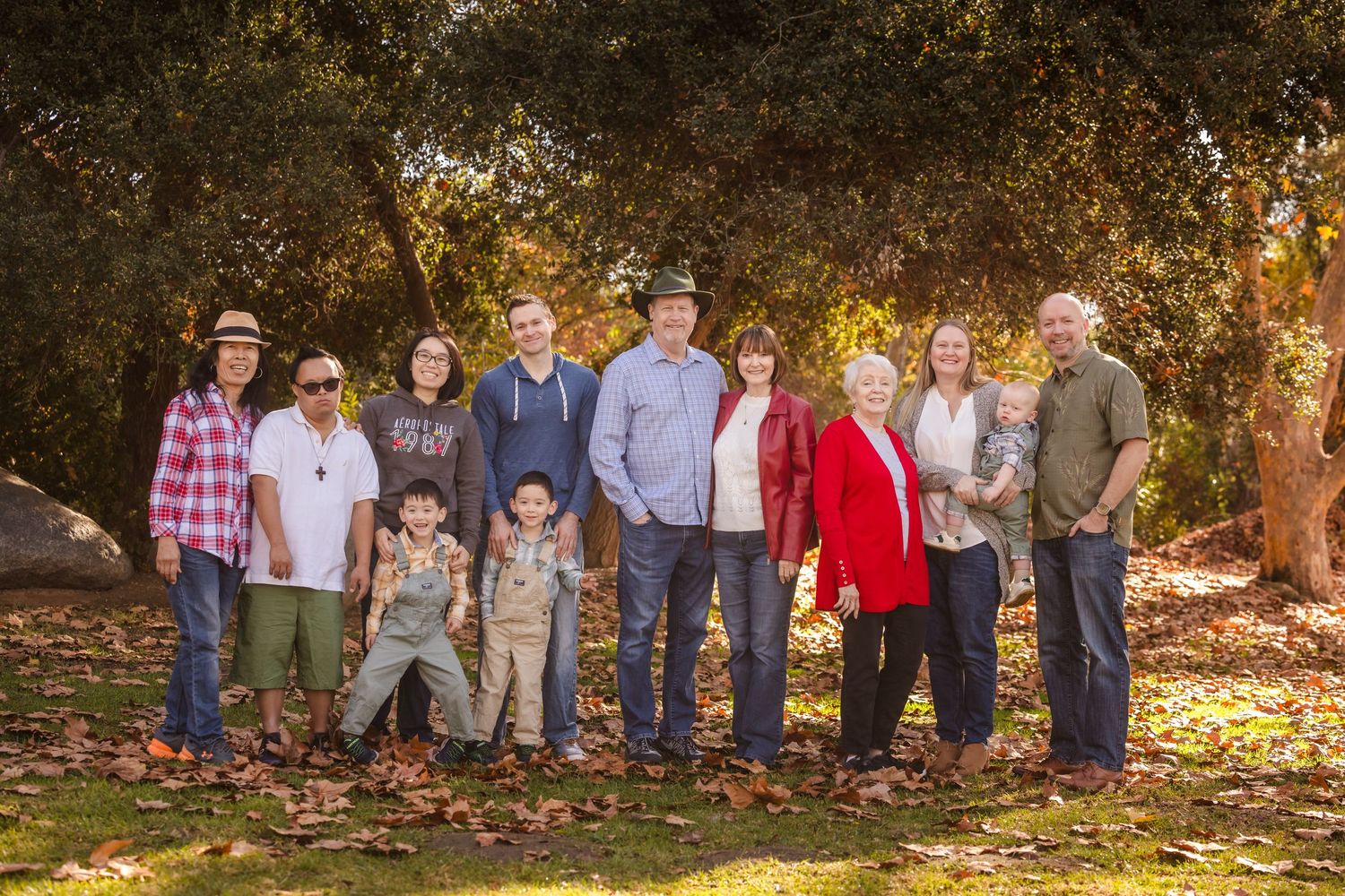 Extended family group poses together for portrait on fallen leaves in autumn setting.