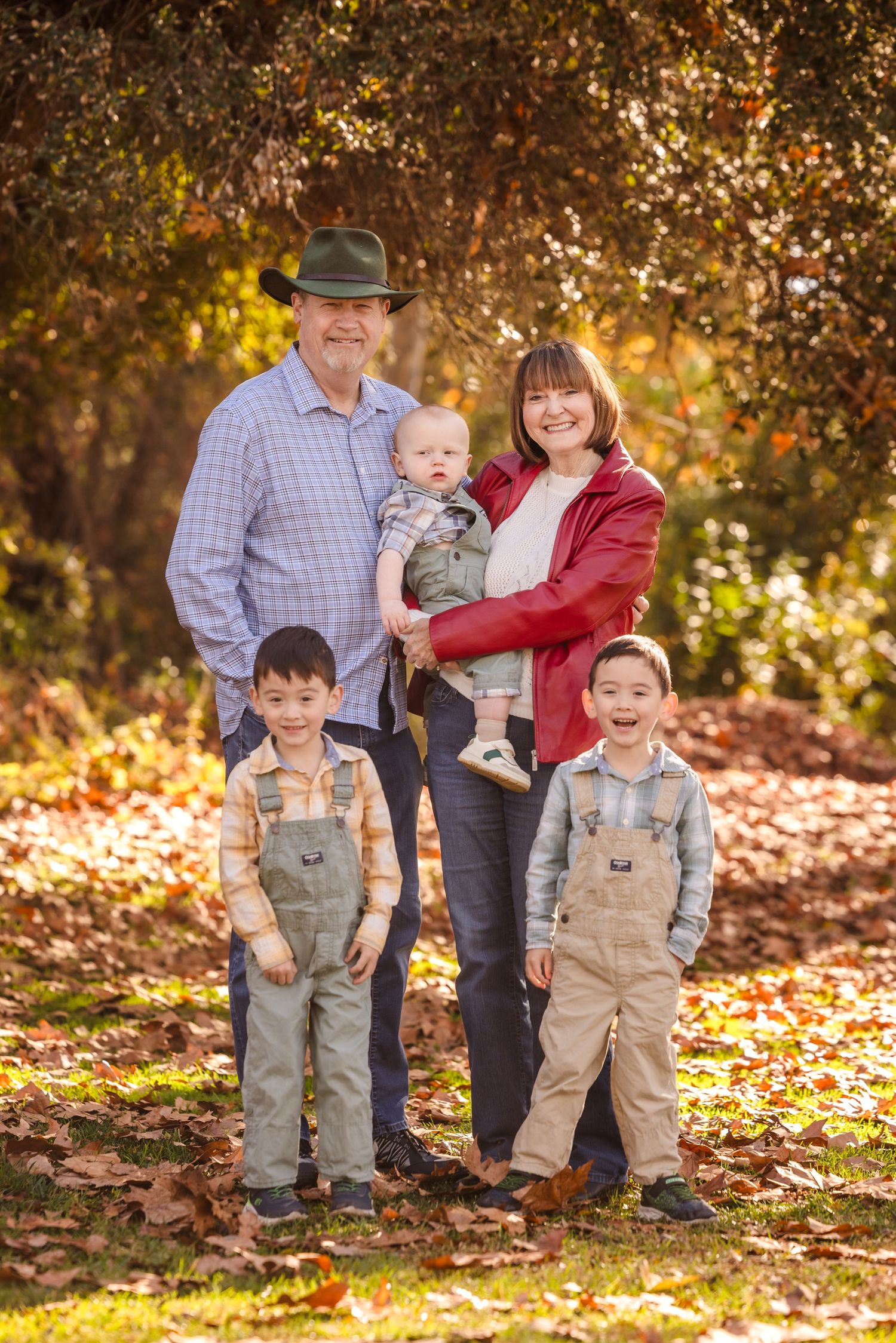 Family of five poses for portrait in autumn setting with fallen leaves.