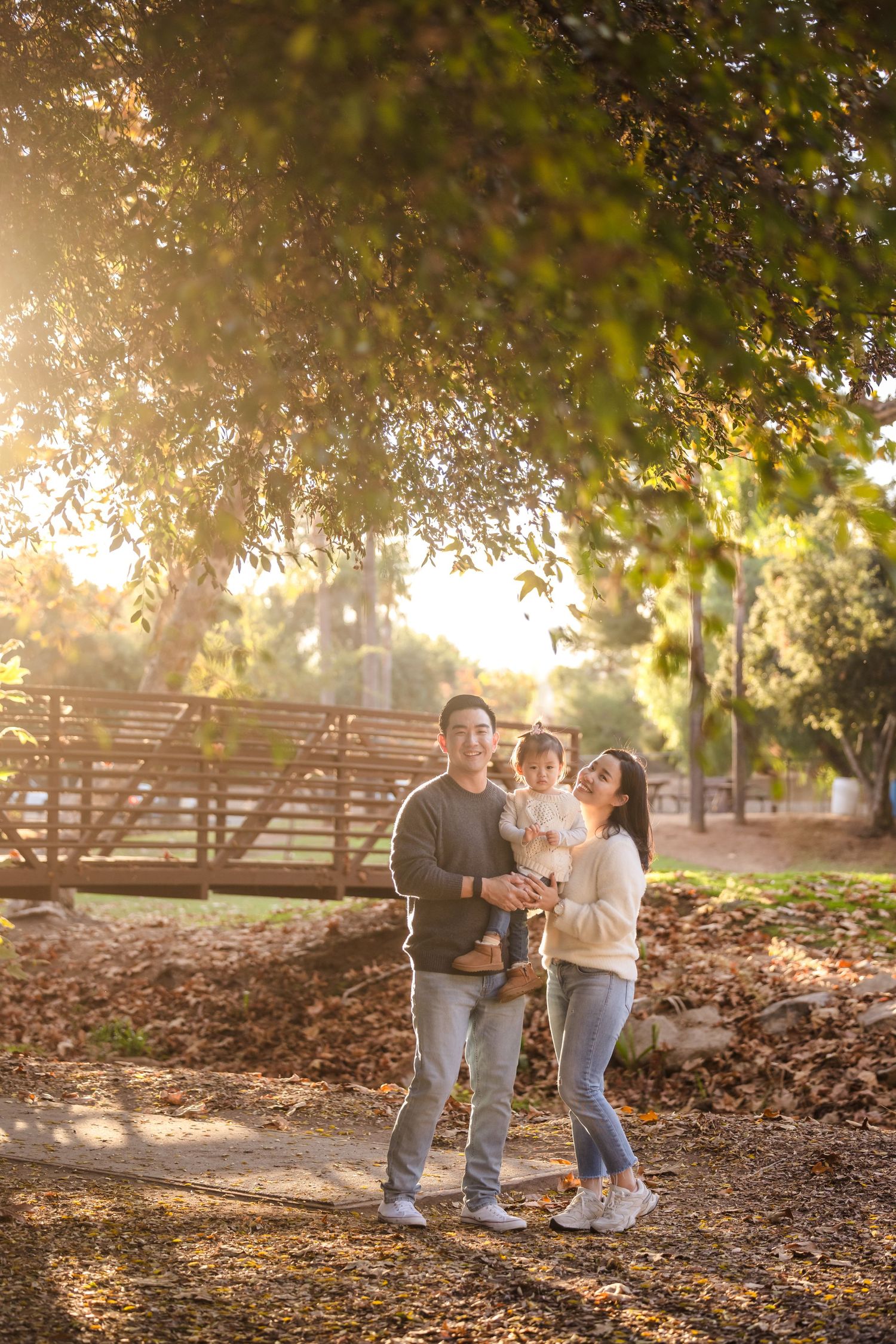 A family enjoys a tender moment together in a sunlit park with golden autumn foliage.