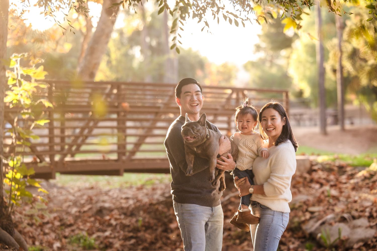 A family stands together on a path surrounded by autumn trees in golden afternoon light.