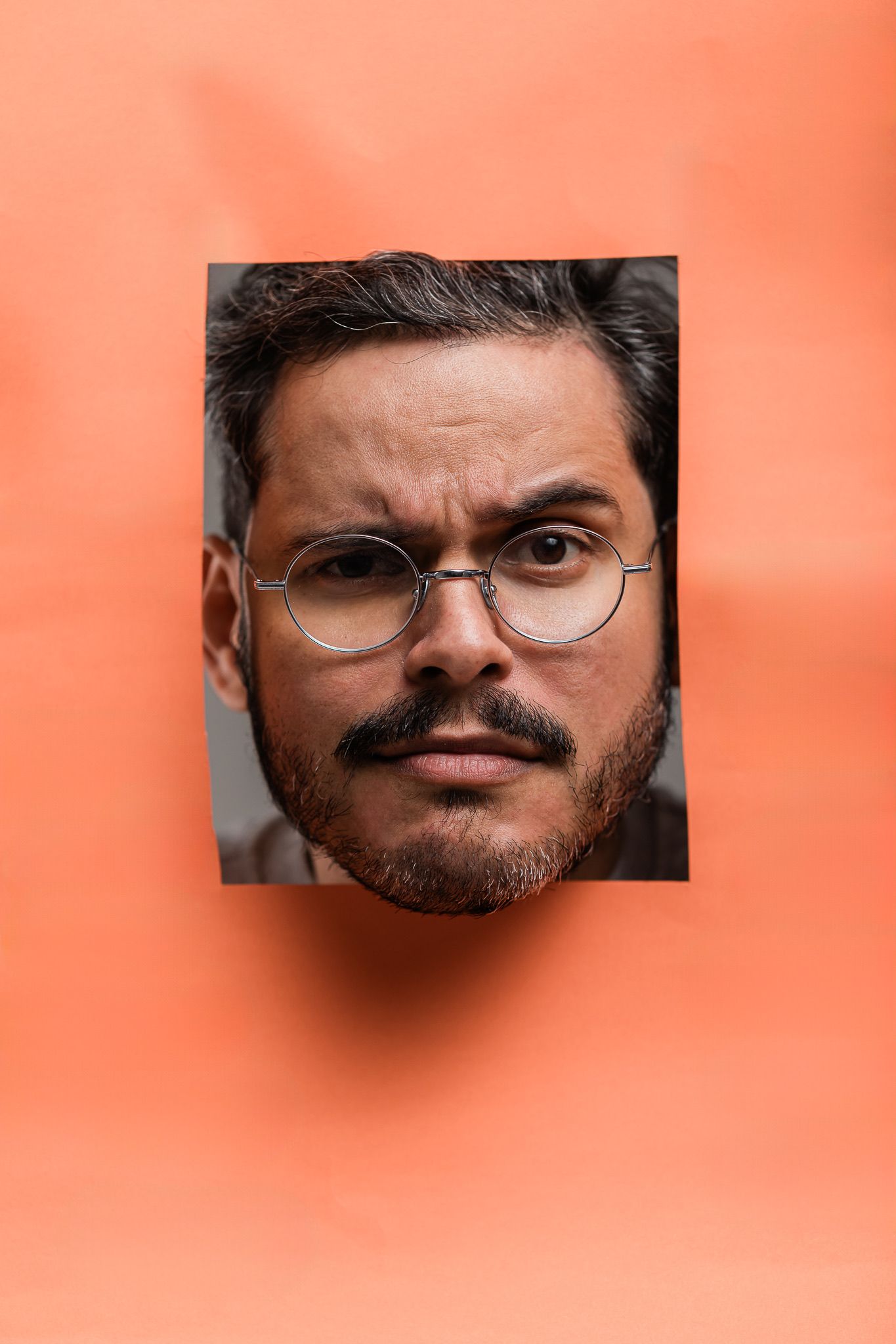 Portrait photograph of a person wearing round glasses against a coral orange background.