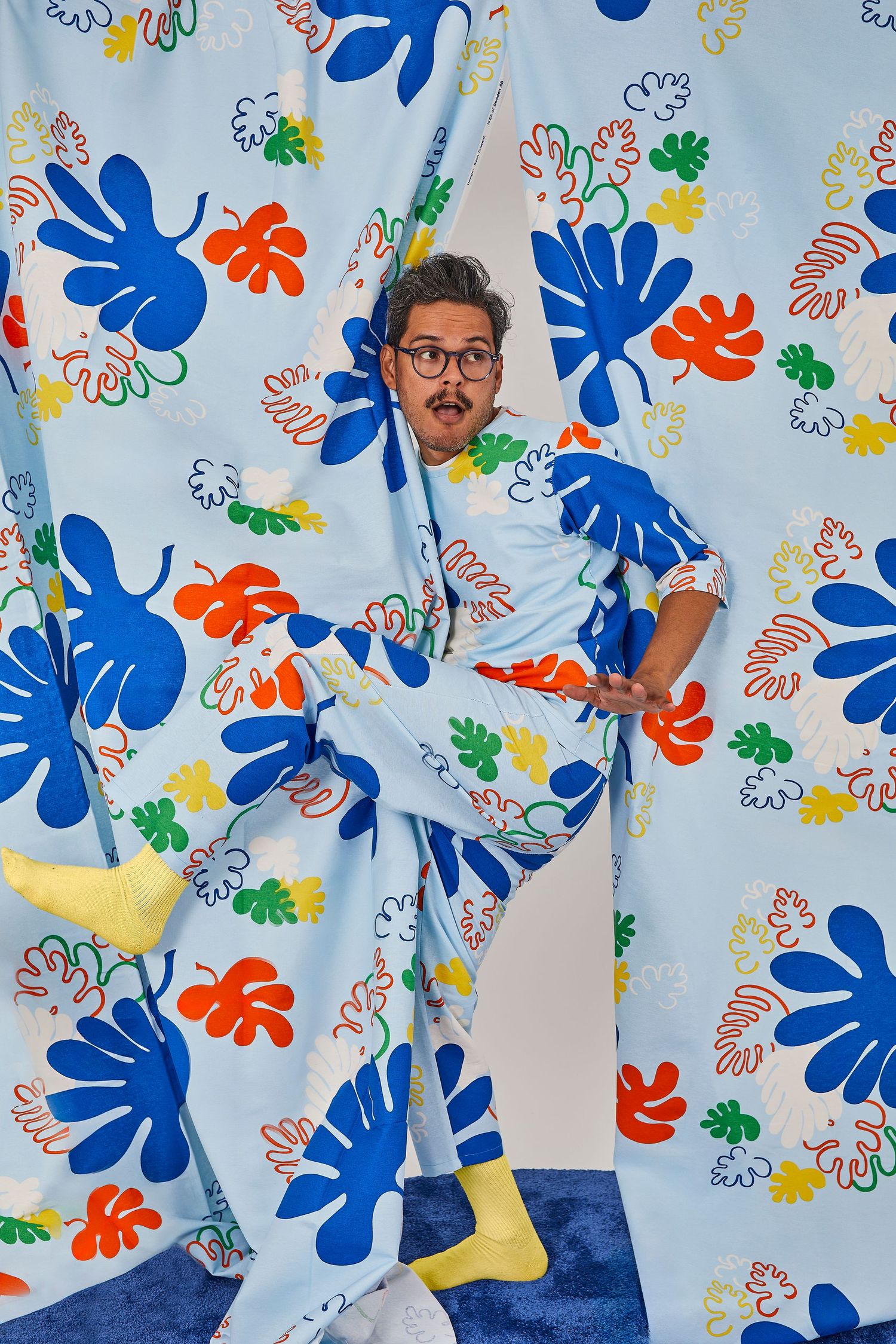 Playful shot of someone peeking through colorful floral patterned curtains while wearing matching pajamas and yellow socks.