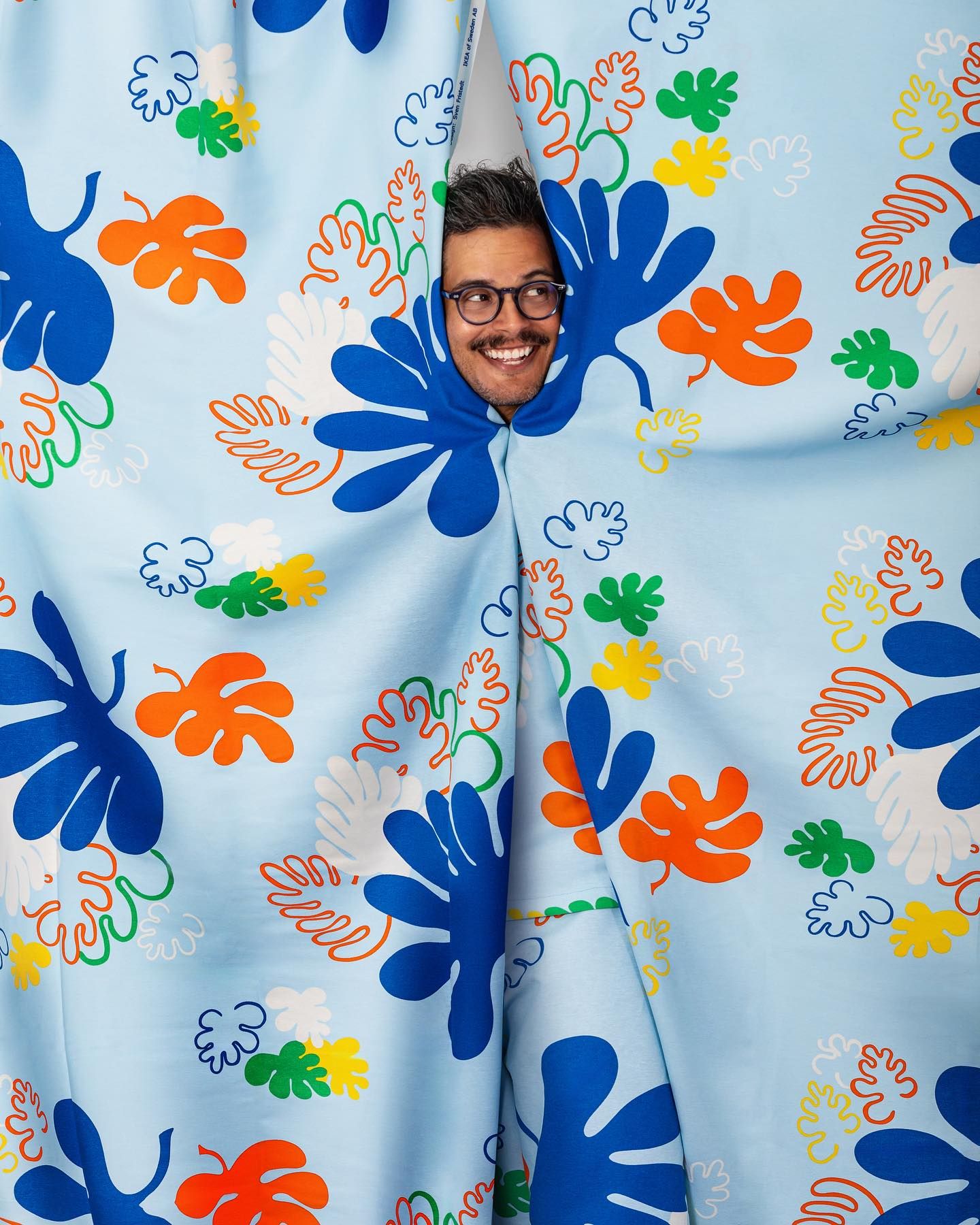 A colorful floral pattern backdrop with blue and orange splatter-style flowers features a playful peek through a cutout.