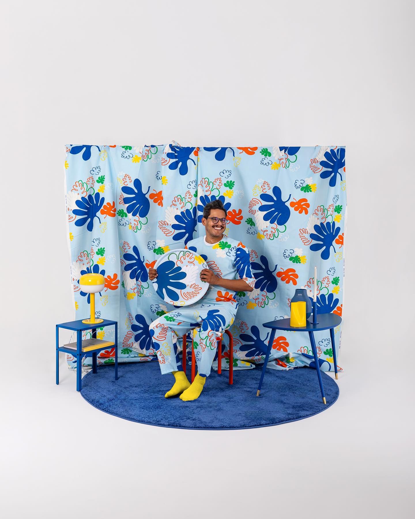 Studio setup with floral backdrop featuring blue flowers, yellow accents, chairs and decorative elements against a light background.