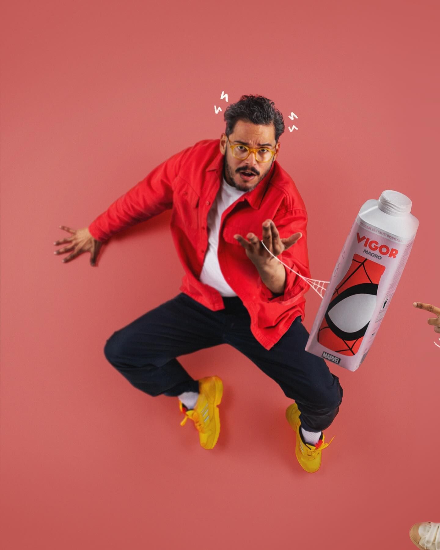 A person in a red jacket and dark pants jumps energetically against a pink background while holding a large water bottle.