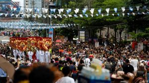 A large crowd gathers under white banners and bunting at an outdoor festival.