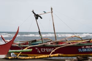 Traditional wooden fishing boats with outriggers lined up along a tropical beach.