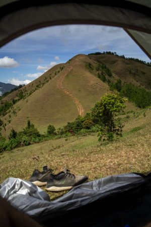 Rolling green hills and mountain trails viewed from inside a tent with camping gear visible.