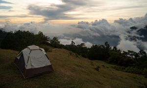 Panoramic view of camping tents on a mountain ridge at sunset with dramatic cloud formations.