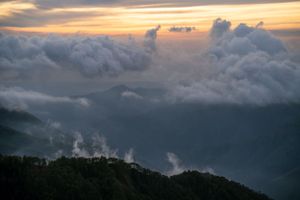 Misty mountain landscape with clouds catching golden light at sunset.
