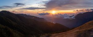 Dramatic sunset over mountain ranges with dark silhouettes and glowing orange clouds in the distance.