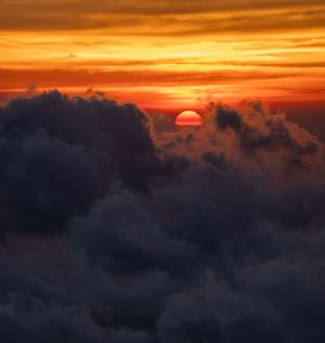 Orange sun peeking through dark storm clouds during a dramatic sunset.