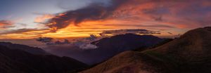 Panoramic mountain landscape under a vibrant orange and purple sunset sky.
