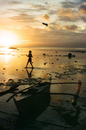Silhouettes of people playing on a beach at sunset with dramatic clouds and ocean waves in the background.
