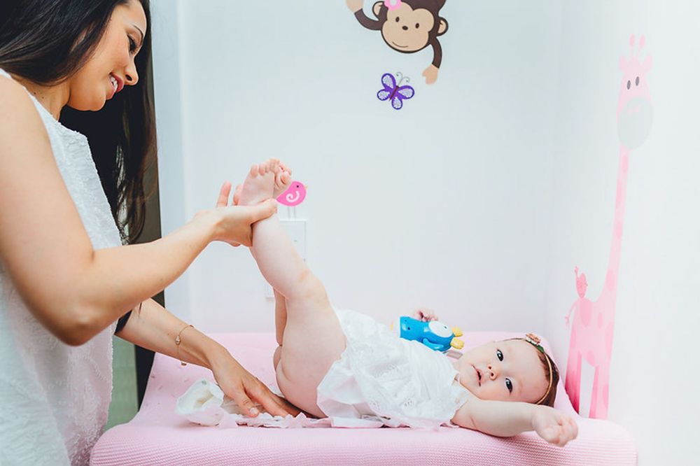 Ein Betreuer wechselt die Windel eines lächelnden Babys auf einem rosa Wickeltisch mit Schmetterlings- und Affen-Wanddekorationen.