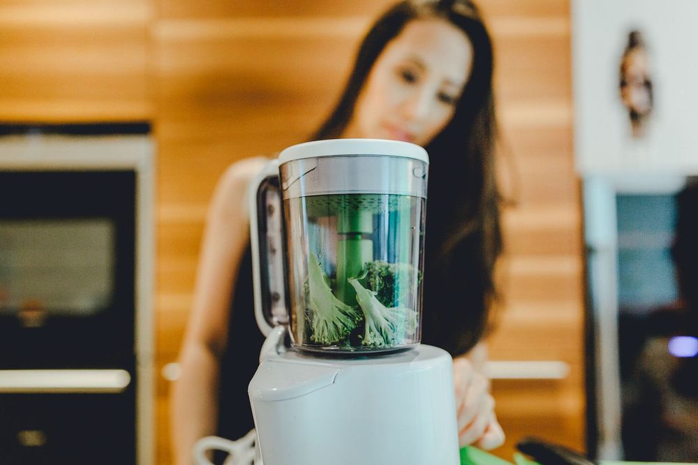 Zutaten für einen grünen Smoothie werden in einem weißen Mixer auf der Holzarbeitsplatte der Küche gemixt.