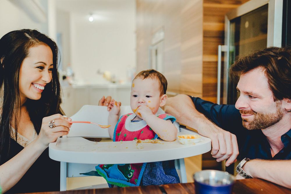 Eine glückliche Familie genießt gemeinsam die Mahlzeit mit ihrem Baby im Hochstuhl zu Hause.