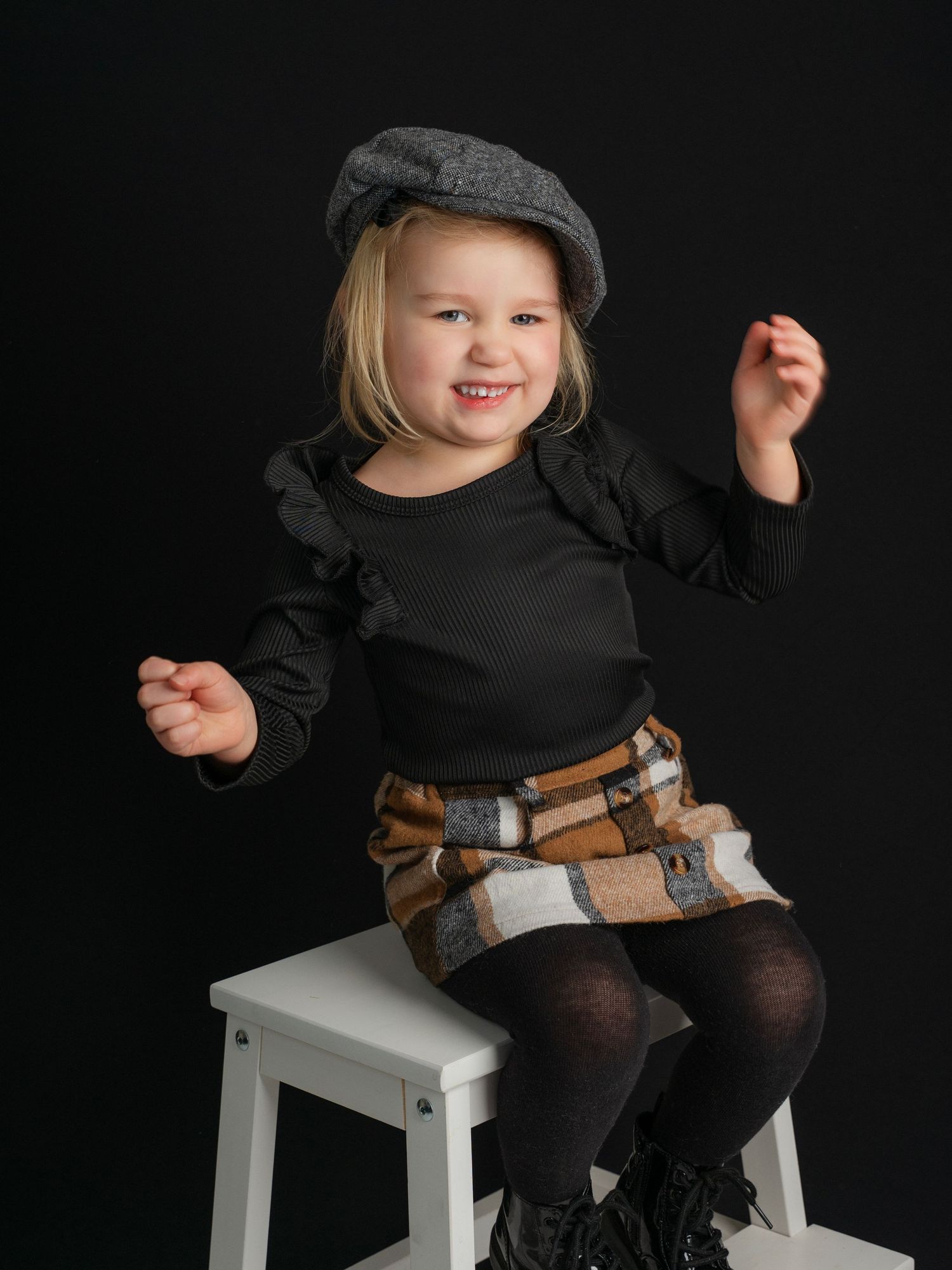 Picture of a little girl sitting on a white stool with pageboy hat and plaid skirt taken by East Tennessee children's photographer