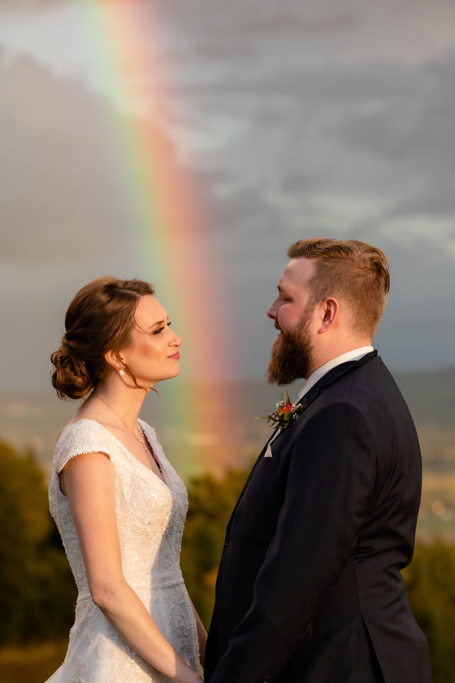 A romantic wedding portrait with a stunning rainbow appearing in the stormy sky behind the couple.