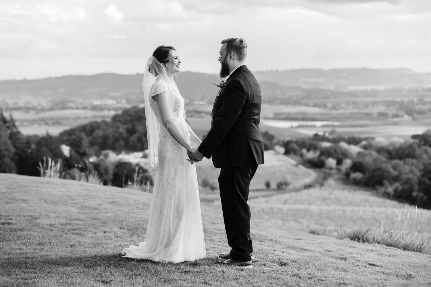 Black and white wedding portrait of a couple standing on a hilltop overlooking a valley.