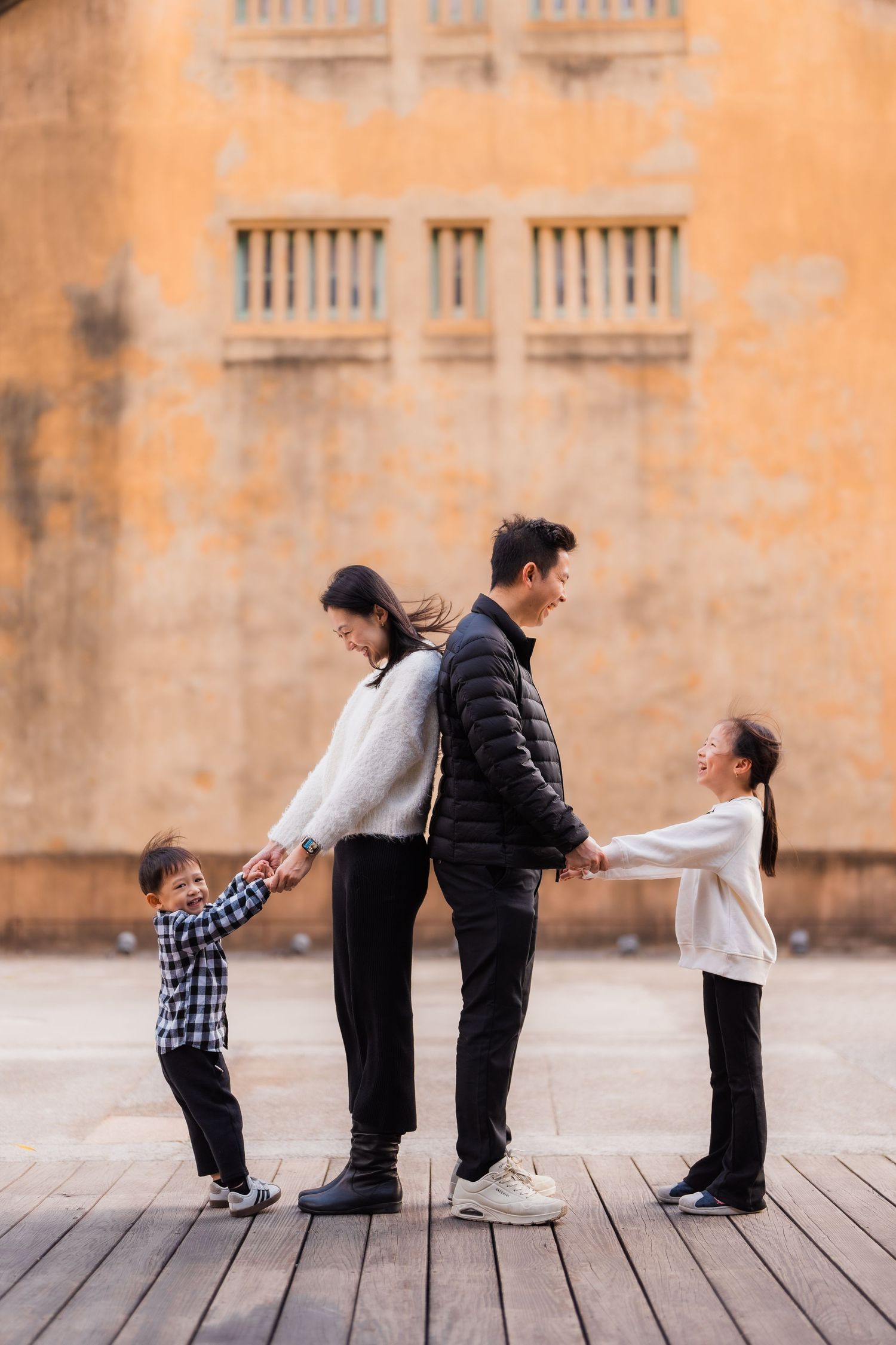 A family creates a playful chain pose on wooden decking against an orange building facade at Huashan 1914 Creative Park.