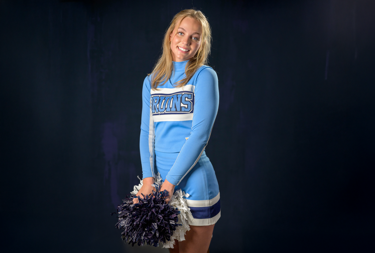 Figure in light blue cheerleader uniform with pom poms against dark background.