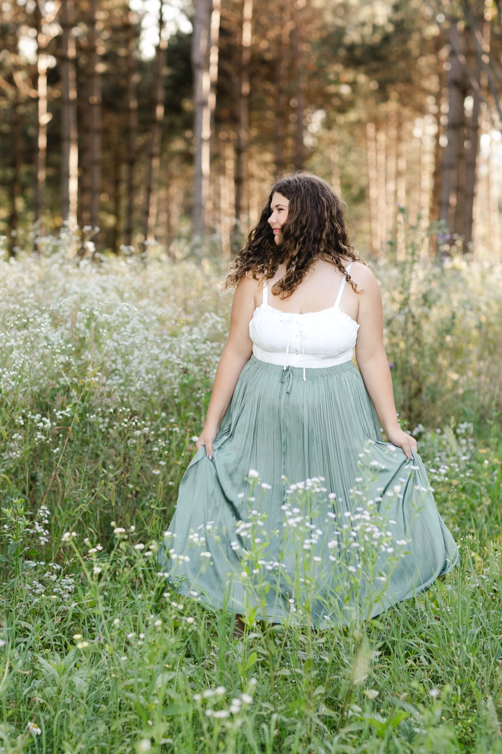 Portrait session in a meadow featuring a sage green dress among white wildflowers.
