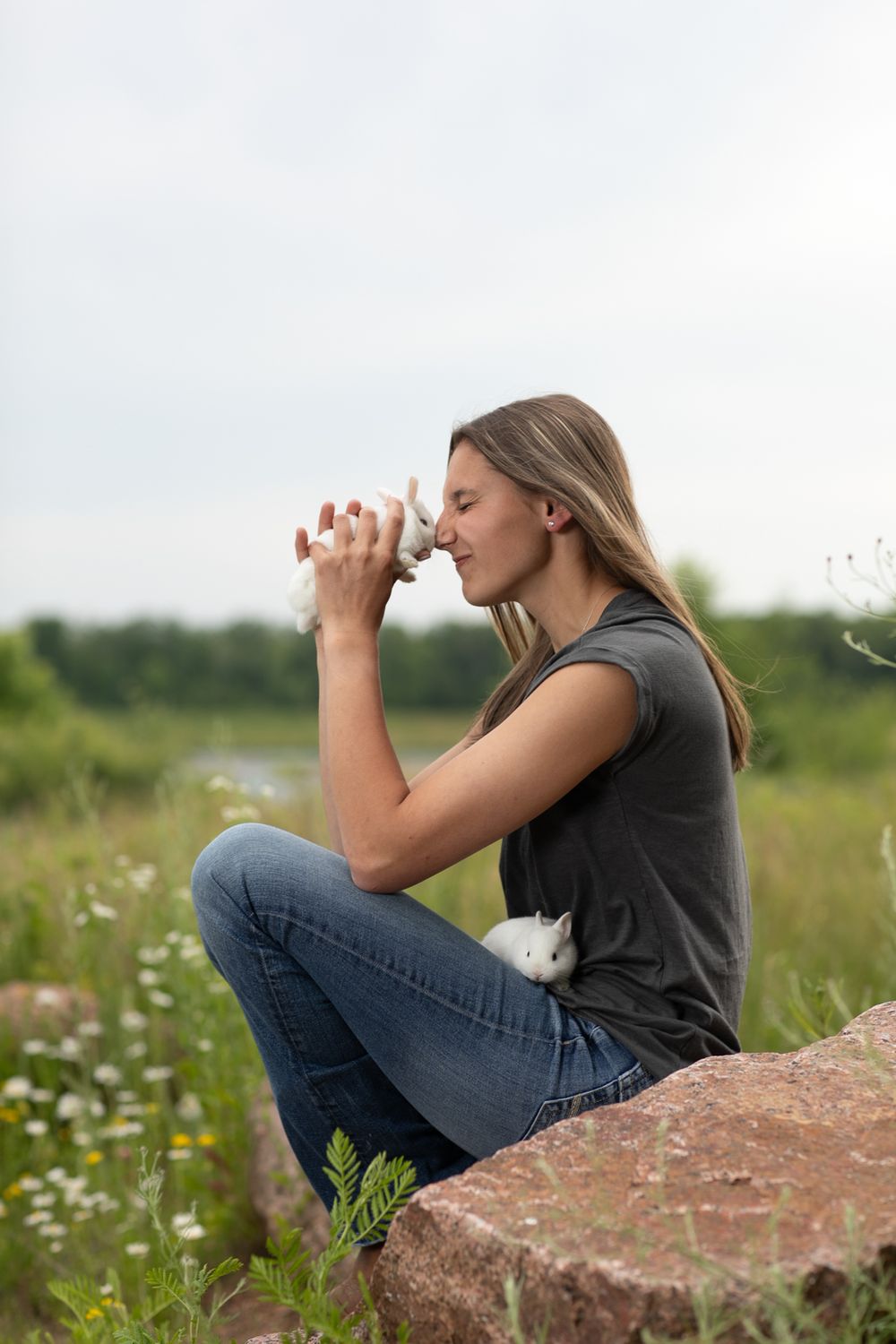 Outdoor portrait sitting on rock formation in field of wildflowers.