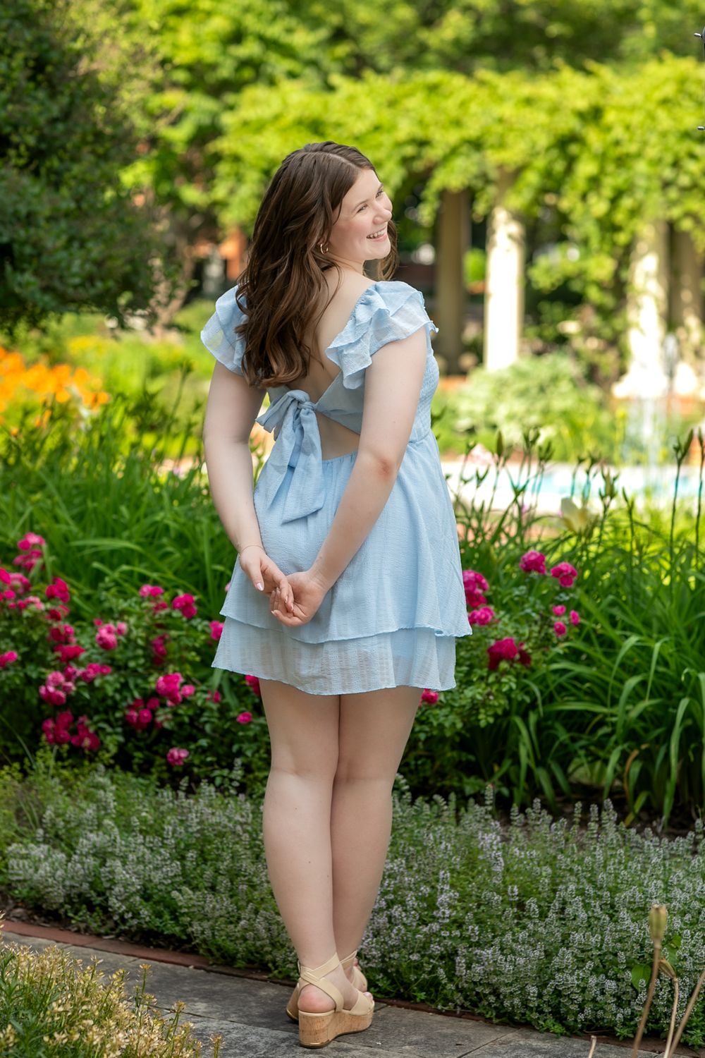 Garden portrait in light blue dress among pink flowers and greenery.