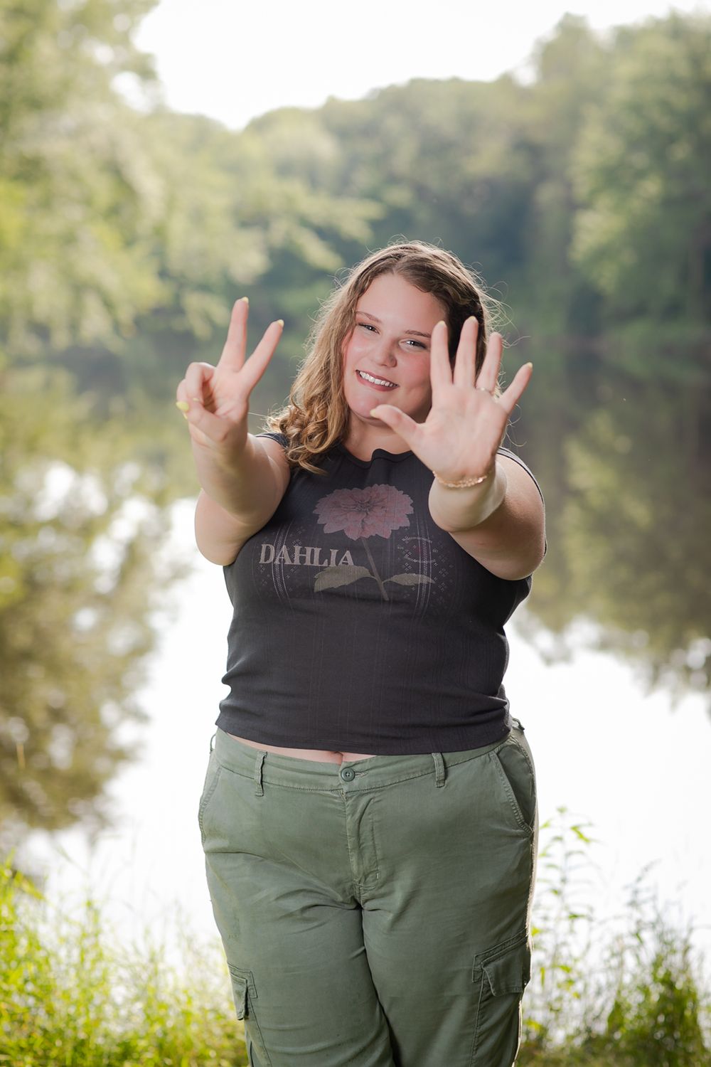 Casual outdoor portrait by lake showing peace signs and joyful expression.