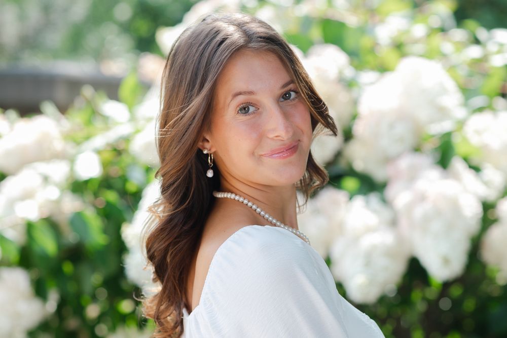 Elegant portrait pose against white flowering bushes in garden setting.