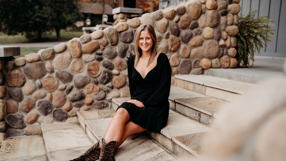 Woman in black dress sitting on stone steps during fall season.