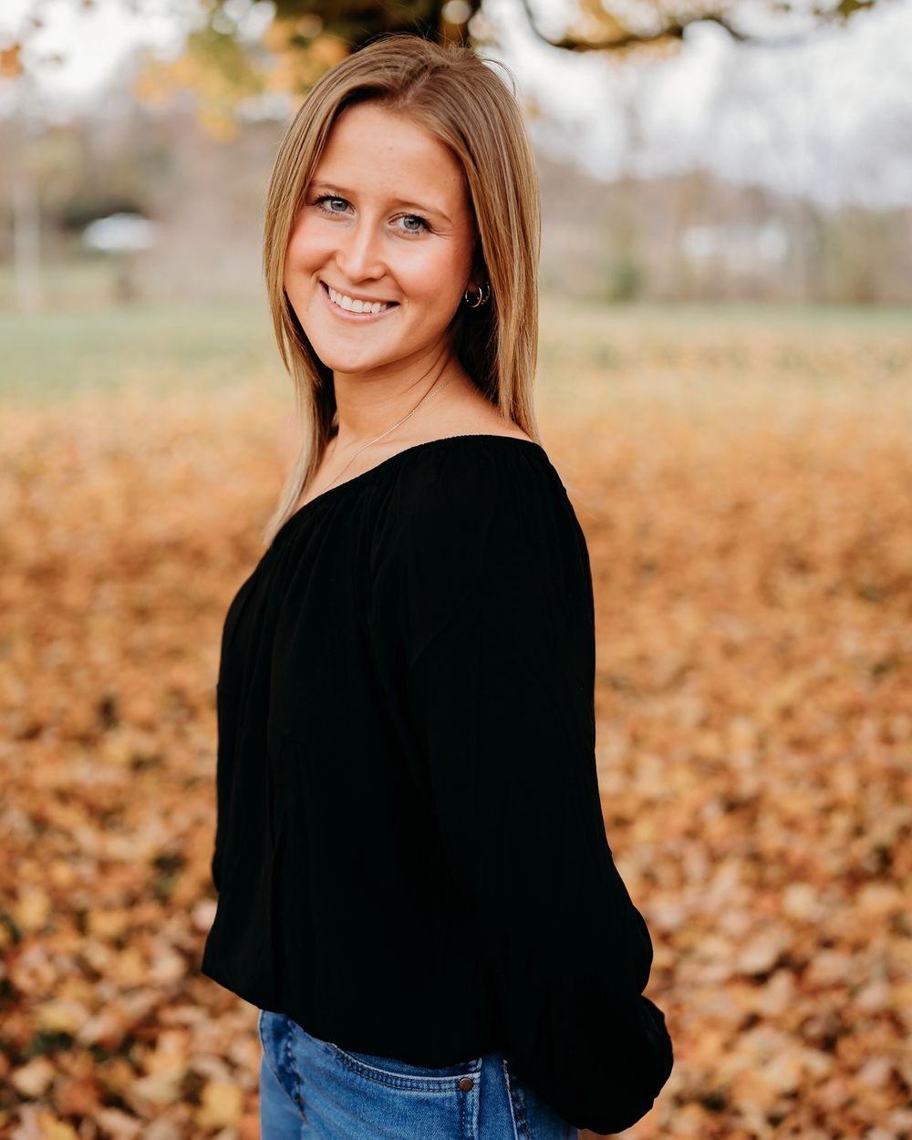 Portrait of woman in black sweater against autumn background with fallen leaves.