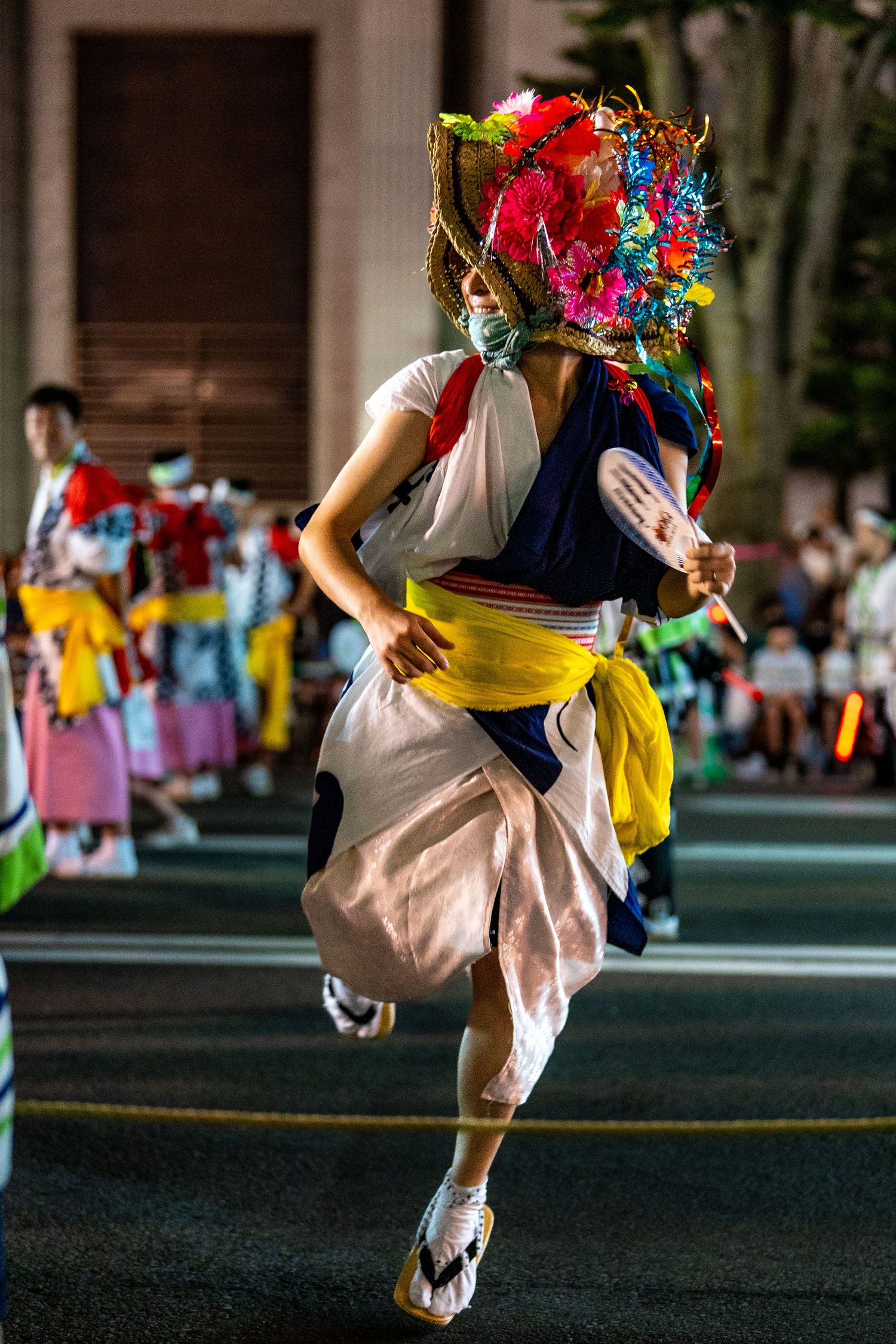 Performer in traditional Japanese festival costume with colorful headdress dances in street parade.