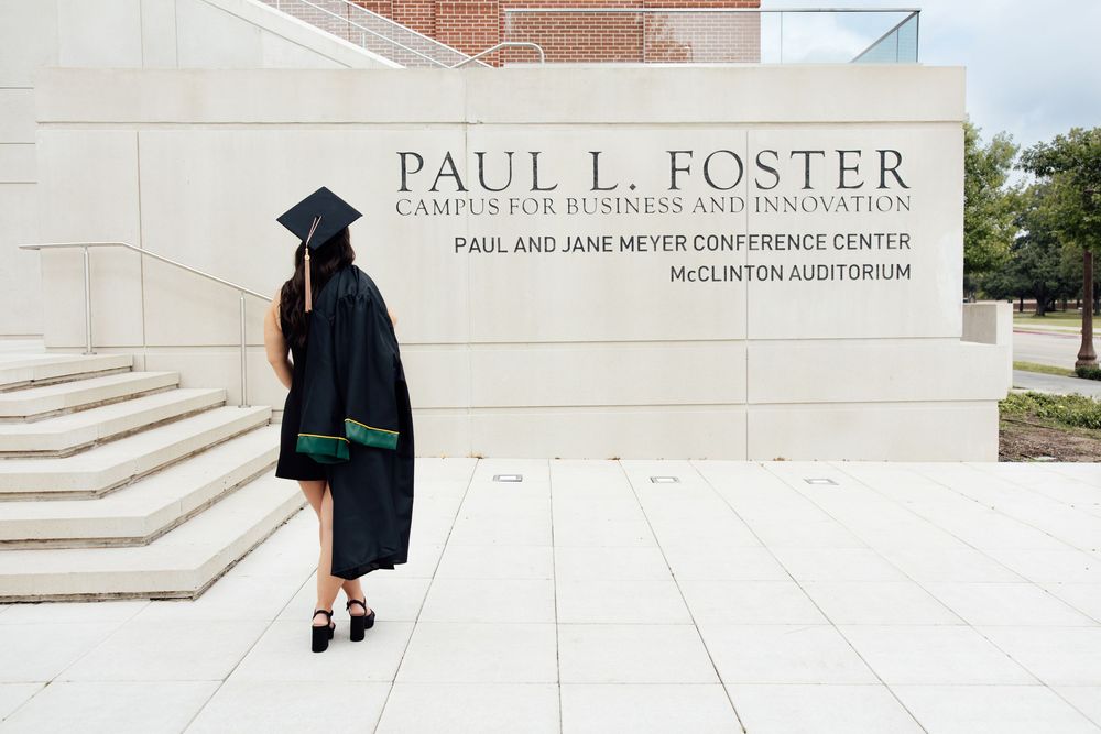 Graduate in cap and gown poses at Paul L. Foster Campus for Business and Innovation at TCU.