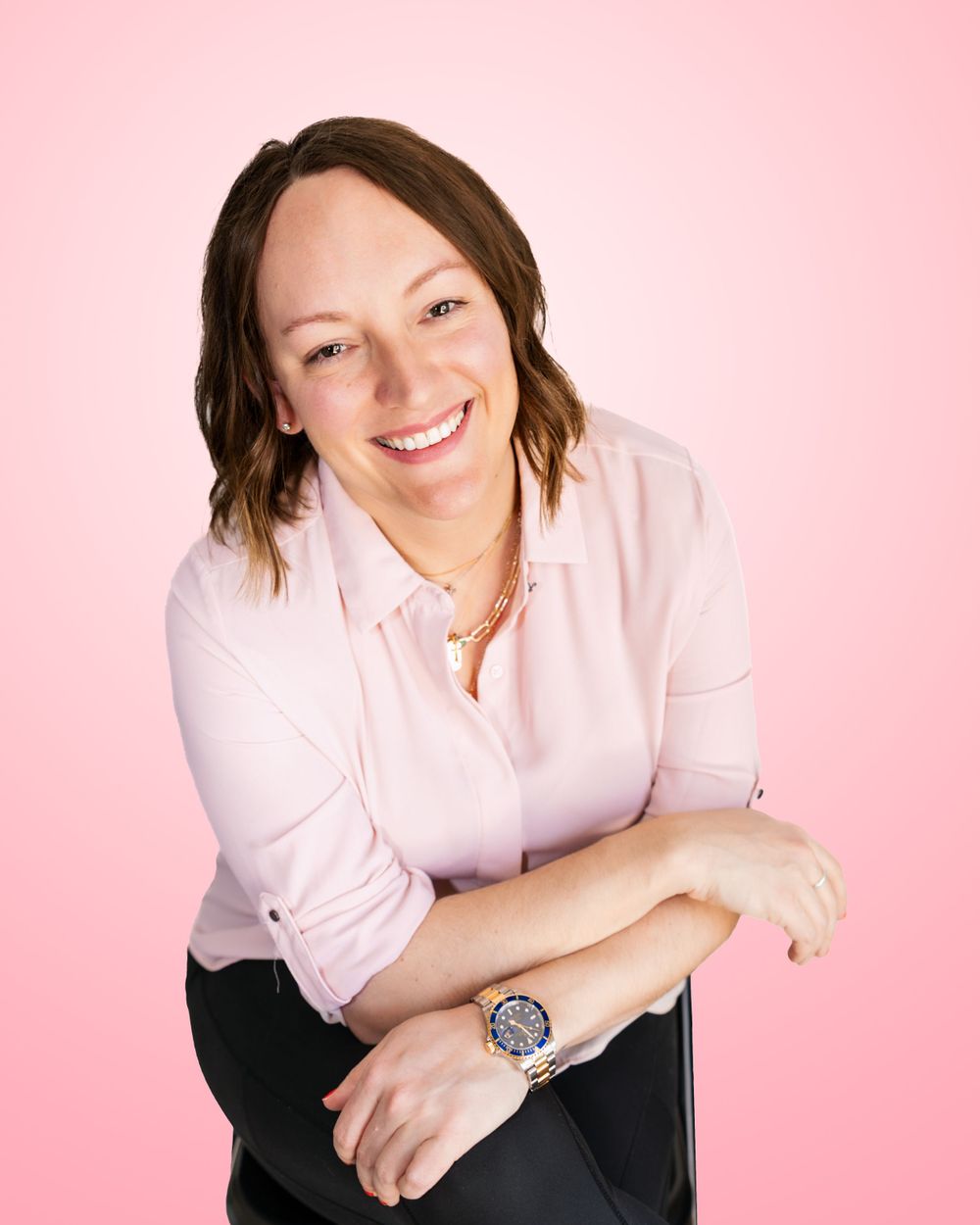 Cheerful woman in pink blouse with watch smiling against pink background.