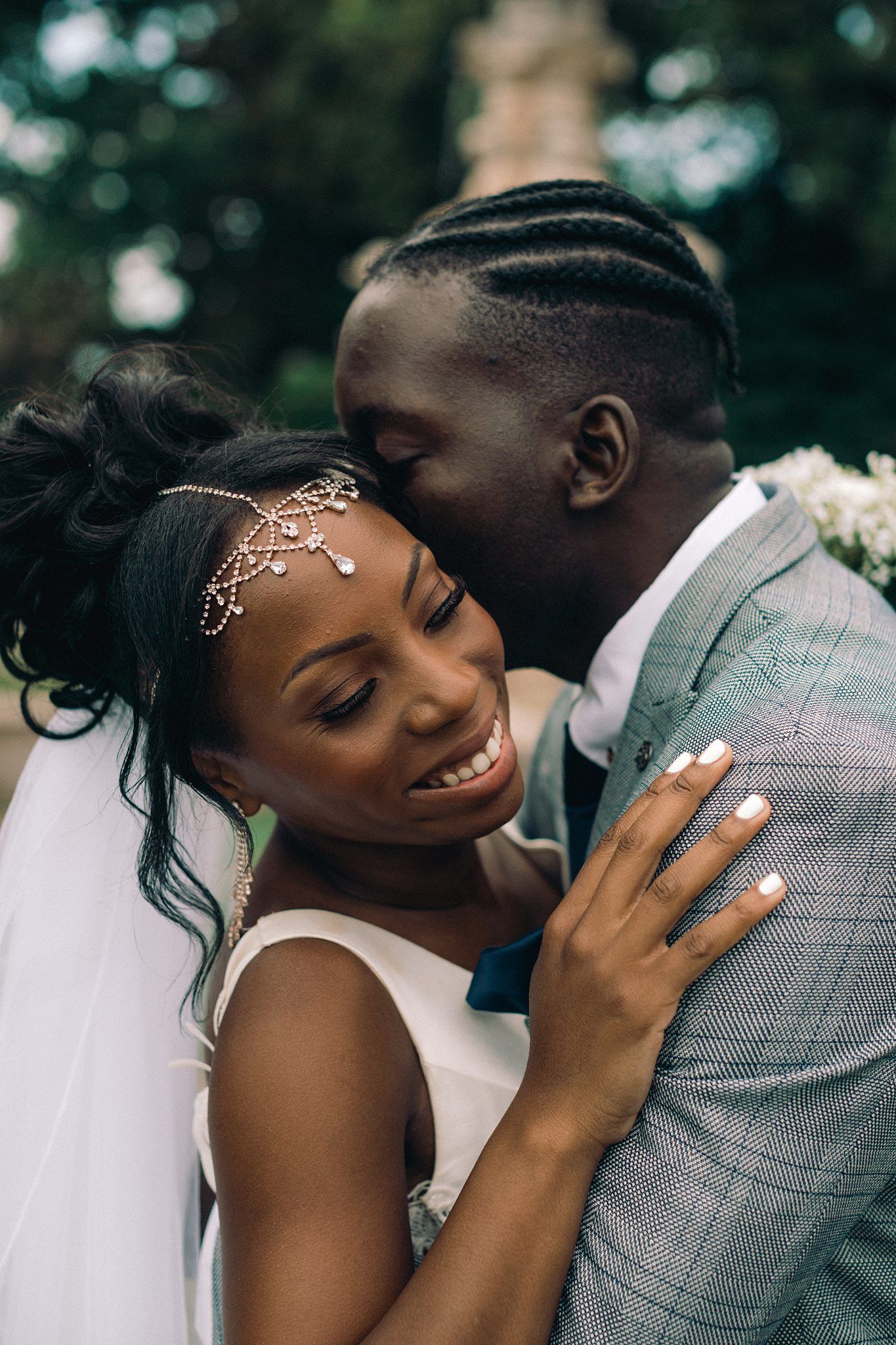 Bride with delicate forehead jewellery and white veil smiles joyfully while embracing husband in grey suit during Halifax wedding photograph