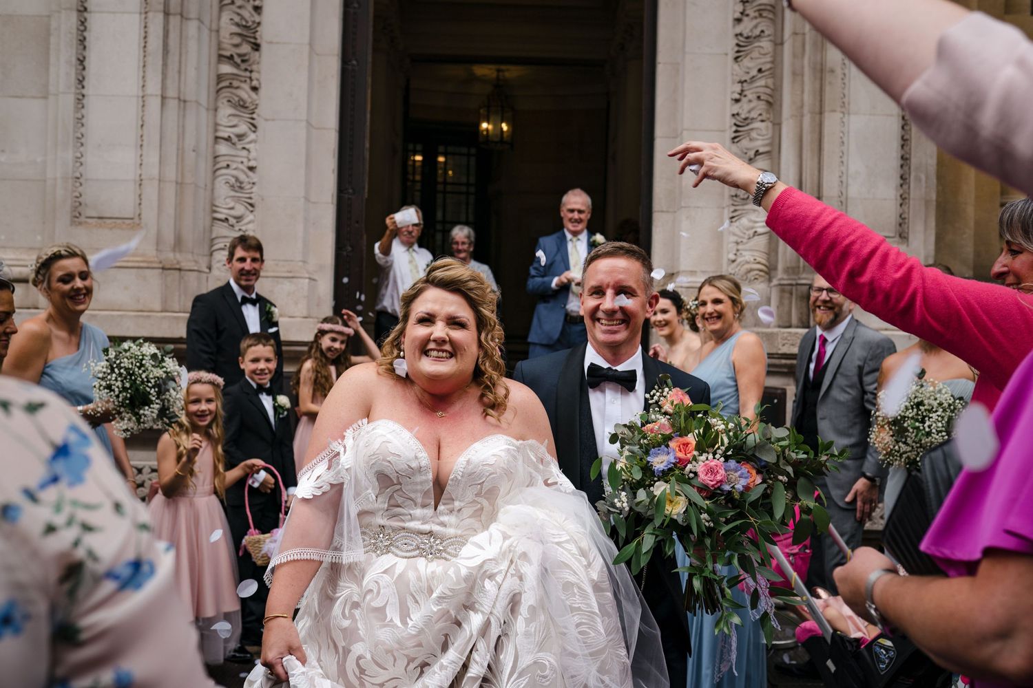 Wedding guests throw confetti as newlyweds exit Halifax, Nova Scotia church in joyful celebration with colorful flowers and bouquets.