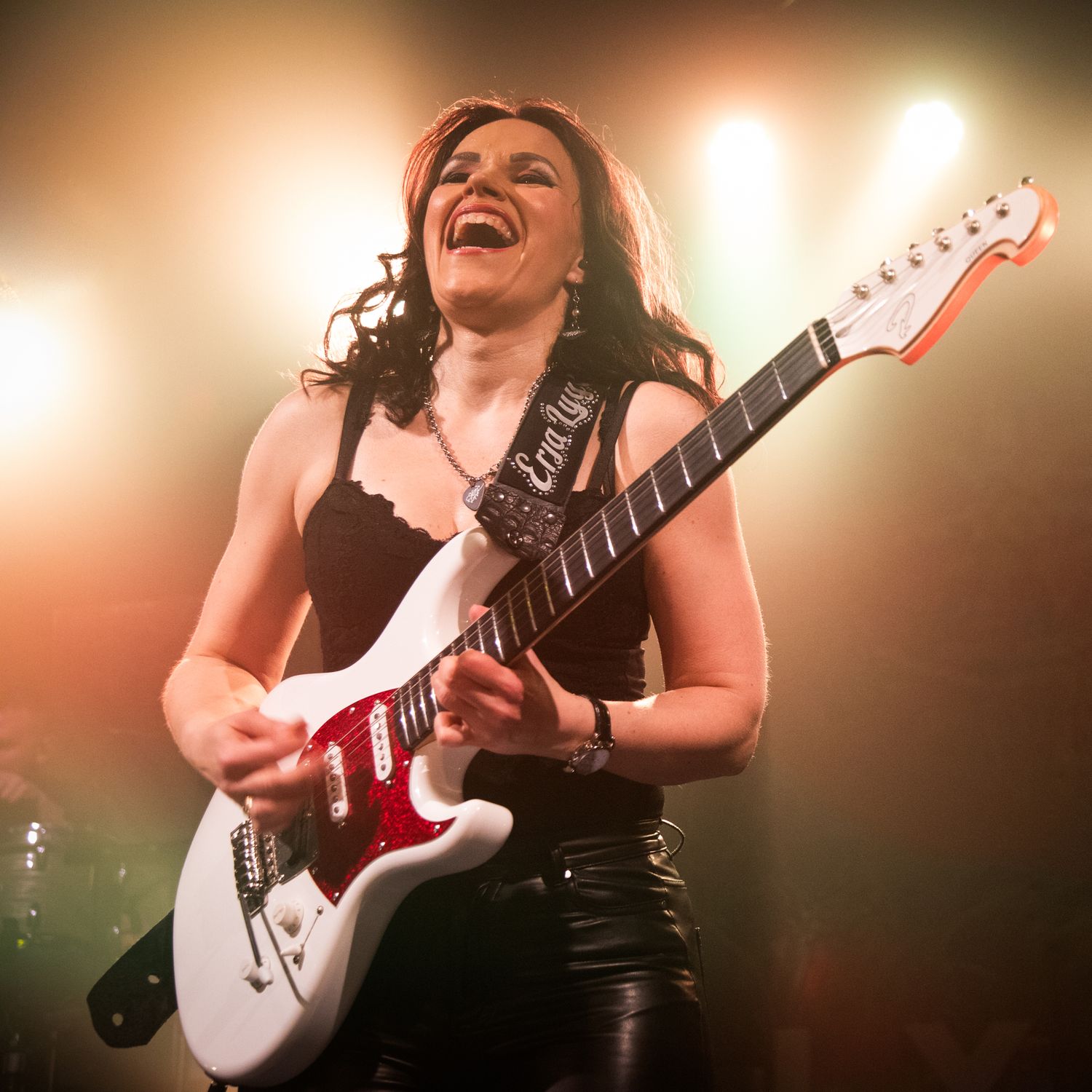 Rock guitarist playing a white electric guitar on stage with warm lighting effects.