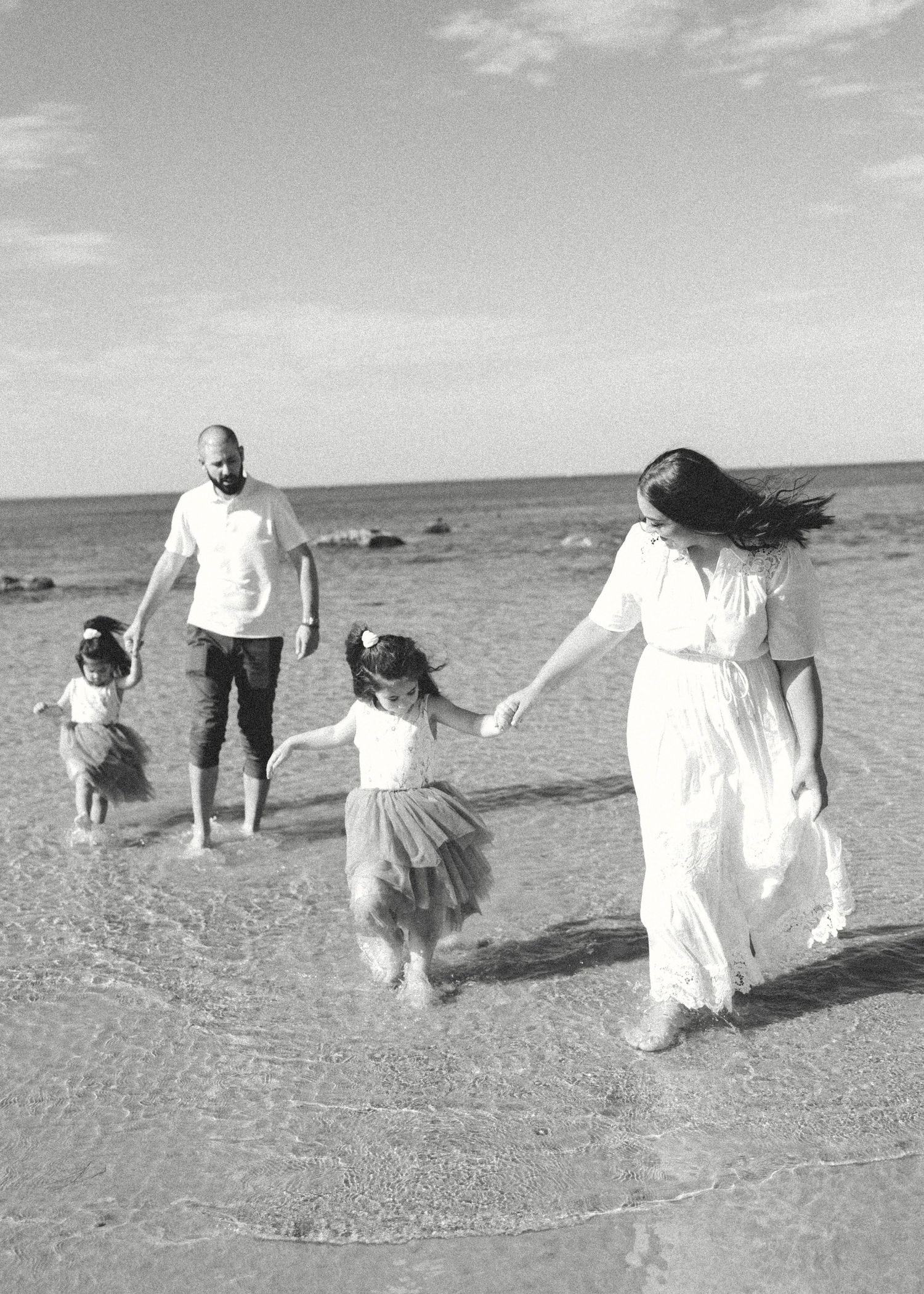 A family wearing matching white shirts stands together in tall golden grass near a waterfront on an overcast day.