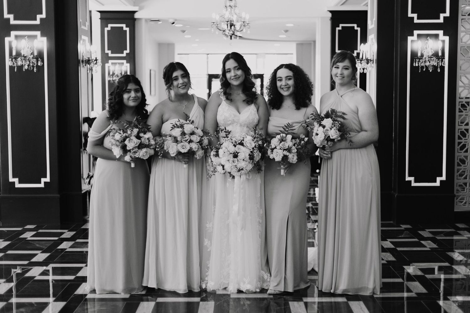 Wedding party in black and white photography pose together in formal attire holding matching floral bouquets.