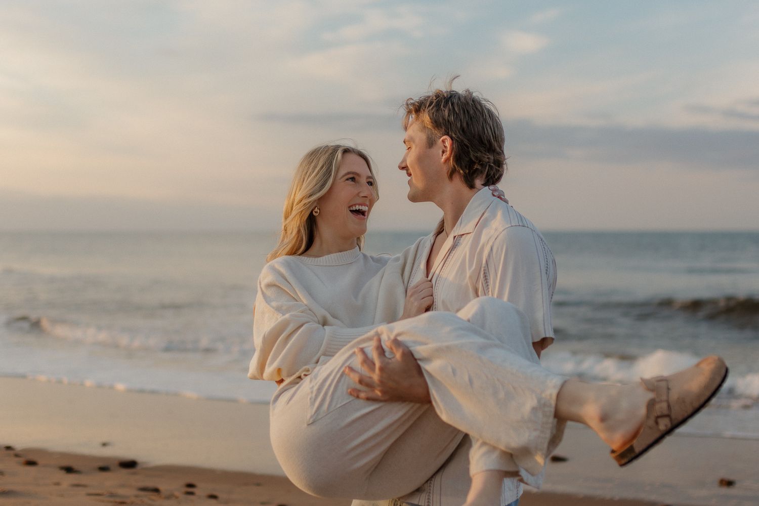 Romantic couple embrace on beach at sunset with soft lighting.