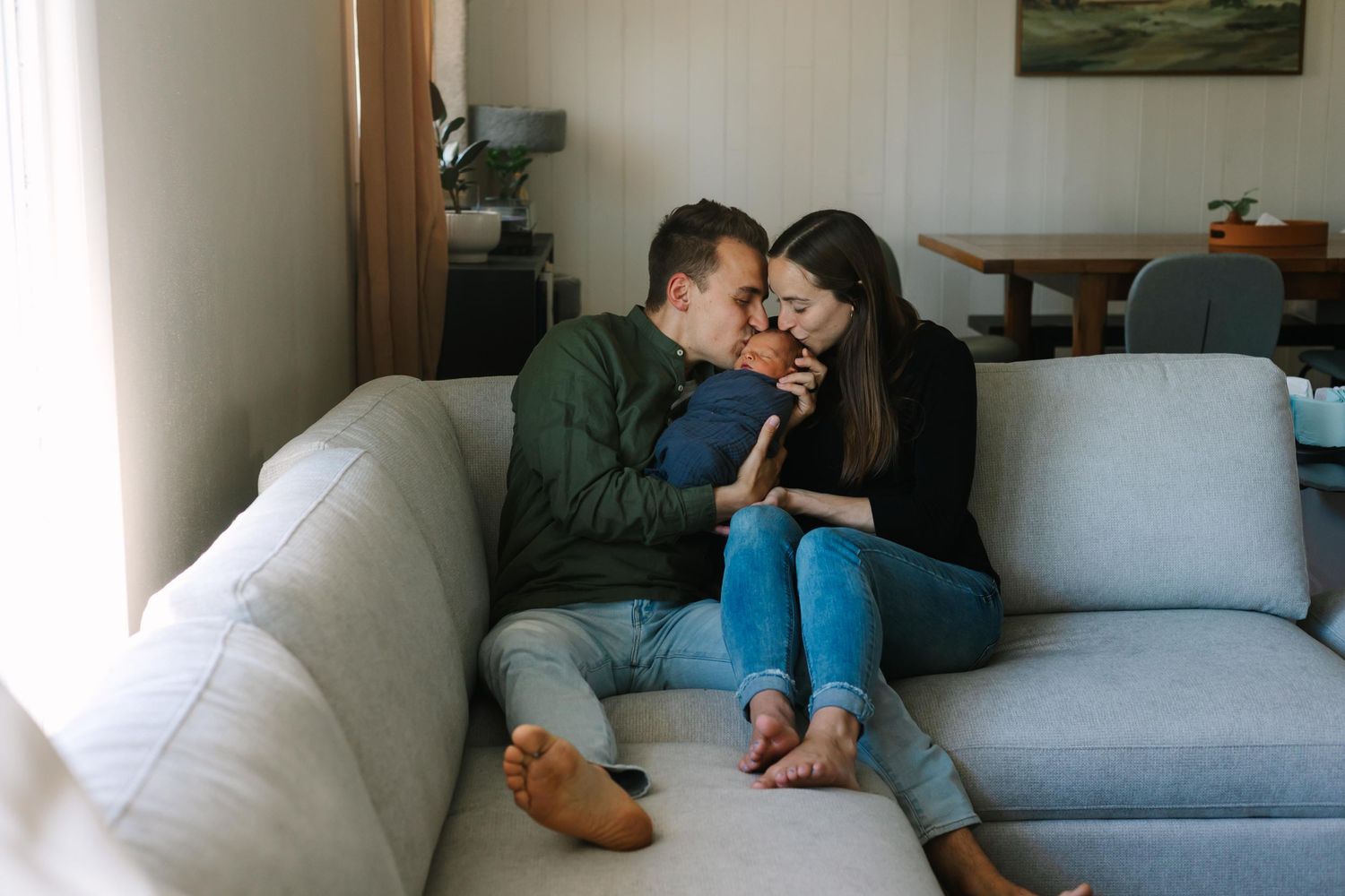 A couple shares an intimate moment while sitting together on a light gray couch in a living room setting.