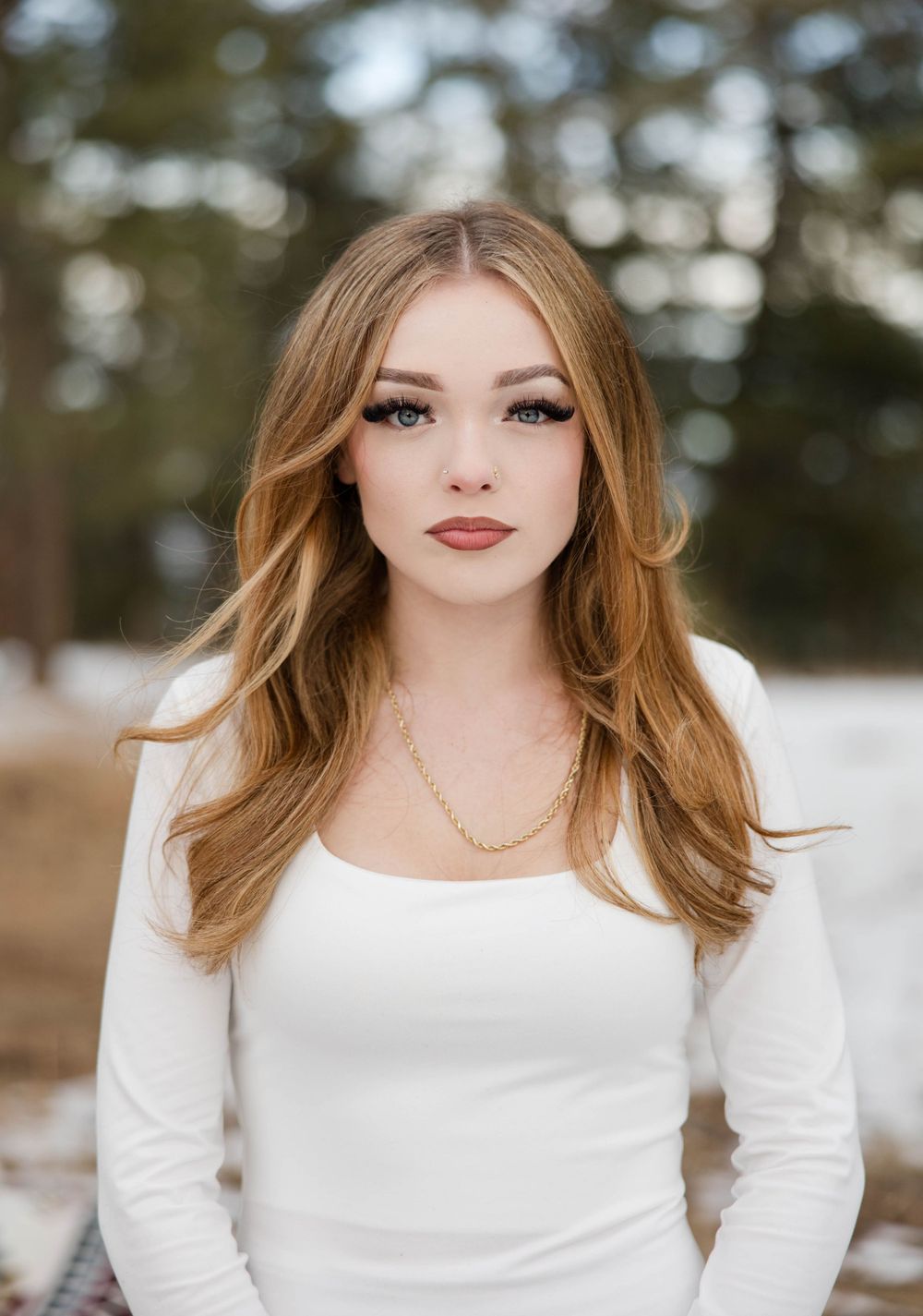 Close up portrait of woman in white top with styled hair against winter background.