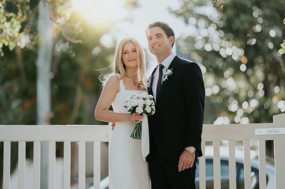 A couple stands together on a white porch railing backdrop during a wedding ceremony with sparkling bokeh lights.